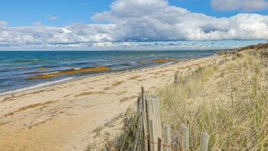 A beach with a wooden fence, sandy shore, and ocean. - Steps to Beach: Timeless Lower Cape Cottage (Brewster)