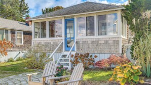 A wooden house with a blue door, a covered porch, and a stone pathway. - Steps to Beach: Timeless Lower Cape Cottage (Brewster)