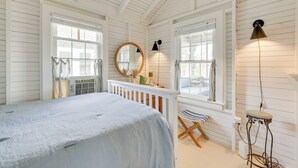 A bedroom with a bed, a window, a mirror, a lamp, and a chair. - Steps to Beach: Timeless Lower Cape Cottage (Brewster)