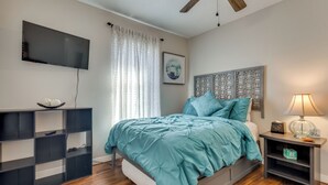 A bedroom with a bed, a TV, a nightstand, a shelf, and a ceiling fan. - Pensacola Condo w/ Patio by Hospitals & Dining (Pensacola)