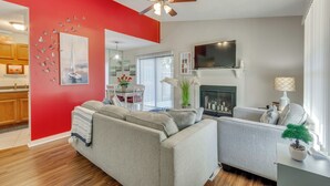 A living room with a red accent wall, a ceiling fan, a fireplace, and a television. - Pensacola Condo w/ Patio by Hospitals & Dining (Pensacola)