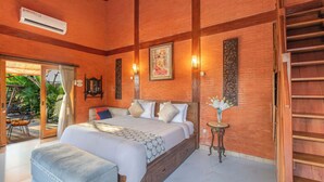 Een ruime slaapkamer met een groot bed, houten balken, een klein tafeltje met bloemen en een trap.
