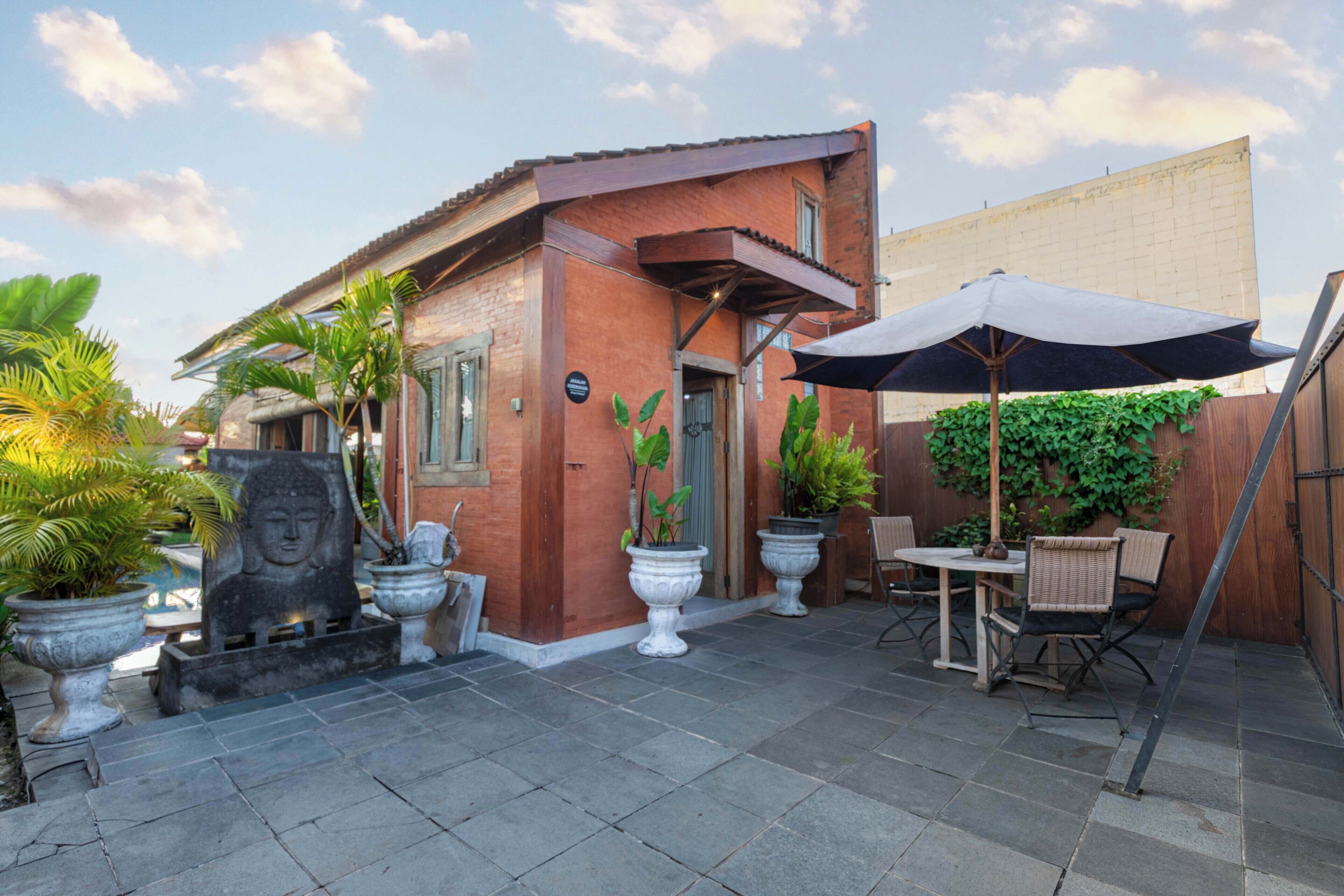 Un patio con mesa y sillas, plantas en macetas y una estatua de Buda.