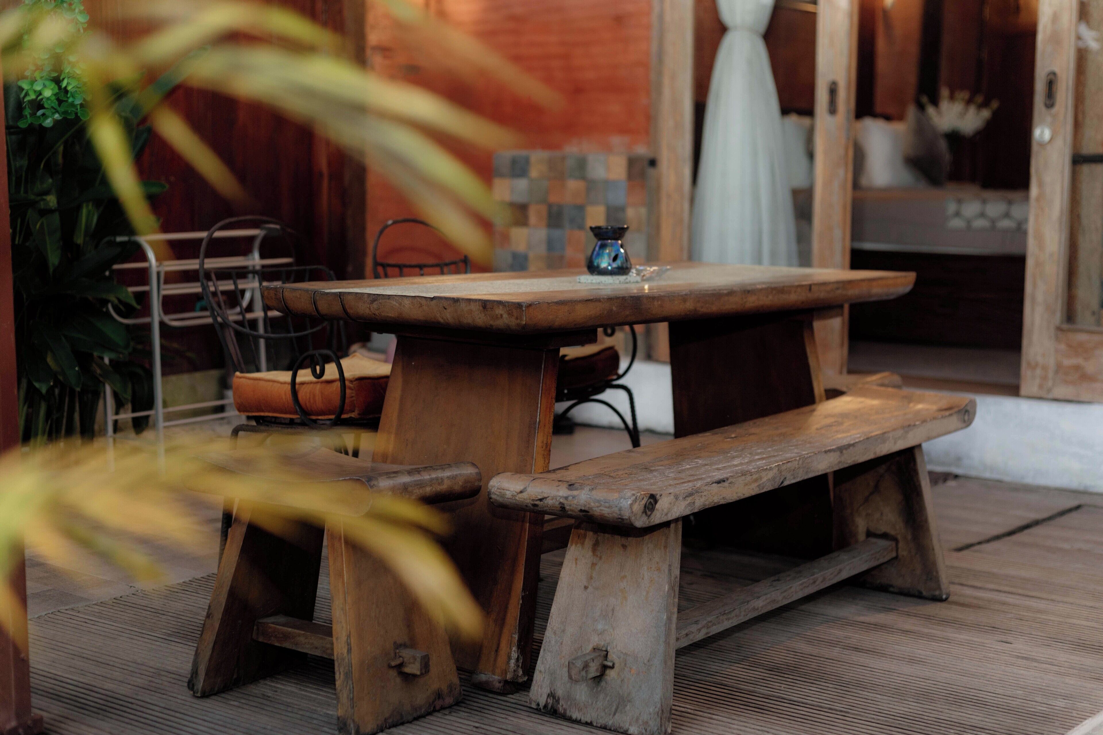 Una mesa de madera rústica con bancos, una silla de metal y un pequeño objeto decorativo sobre la mesa.