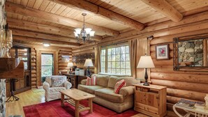 A log cabin interior with a wooden ceiling, a sofa, a coffee table, a lamp, and a stone fireplace. - Along Big Wood River: Hailey Family Cabin w/ Yard (Hailey)