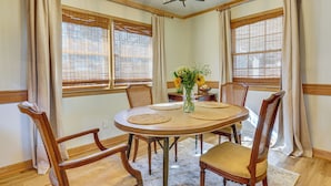 A dining area with a round table, six wooden chairs, a vase with flowers, and windows with blinds. - River, Trails & Wine! Extended Escape Near Mt Airy (Ararat)