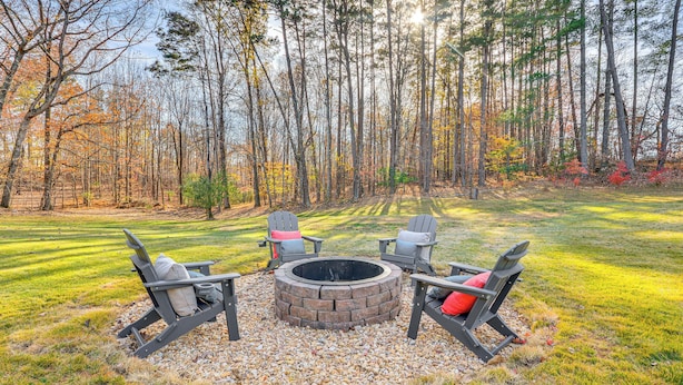 A circular fire pit surrounded by four Adirondack chairs with cushions, set on a gravel area in a grassy field with trees in the background. - River, Trails & Wine! Extended Escape Near Mt Airy (Ararat)