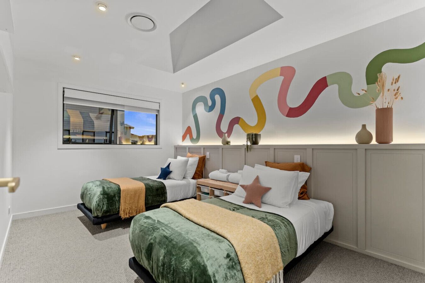 A modern hotel room with two beds, a large abstract wall art piece, a window with a view, and a ceiling light.