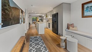 A modern kitchen with a central island, a refrigerator, and a dining area with a bench. - Spacious Coastal Luxe Home with Sea View & Parking (Auckland Hibiscus Coast)