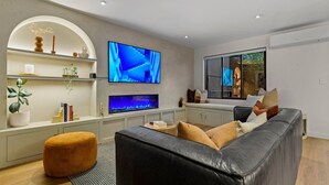 A modern living room with a black leather sofa, a TV, a fish tank, and a large window. - Spacious Coastal Luxe Home with Sea View & Parking (Auckland Hibiscus Coast)