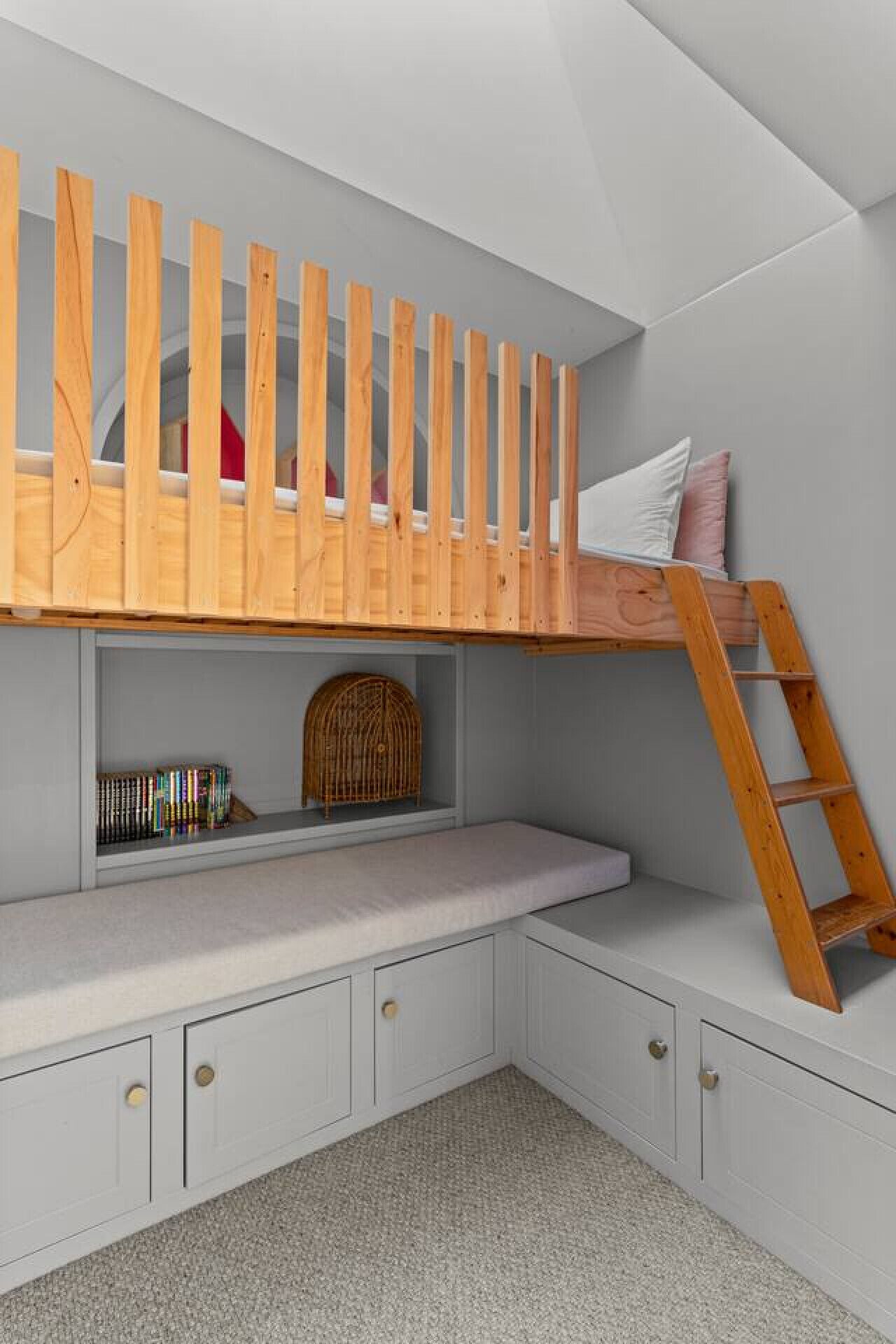 A child's bunk bed with a wooden ladder, a bookshelf, and a decorative birdcage.
