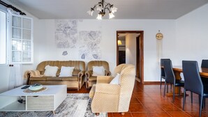 Ein Wohnzimmer mit zwei gemusterten Sofas, einem Couchtisch, einem Esstisch mit Stühlen und einer Pendelleuchte.