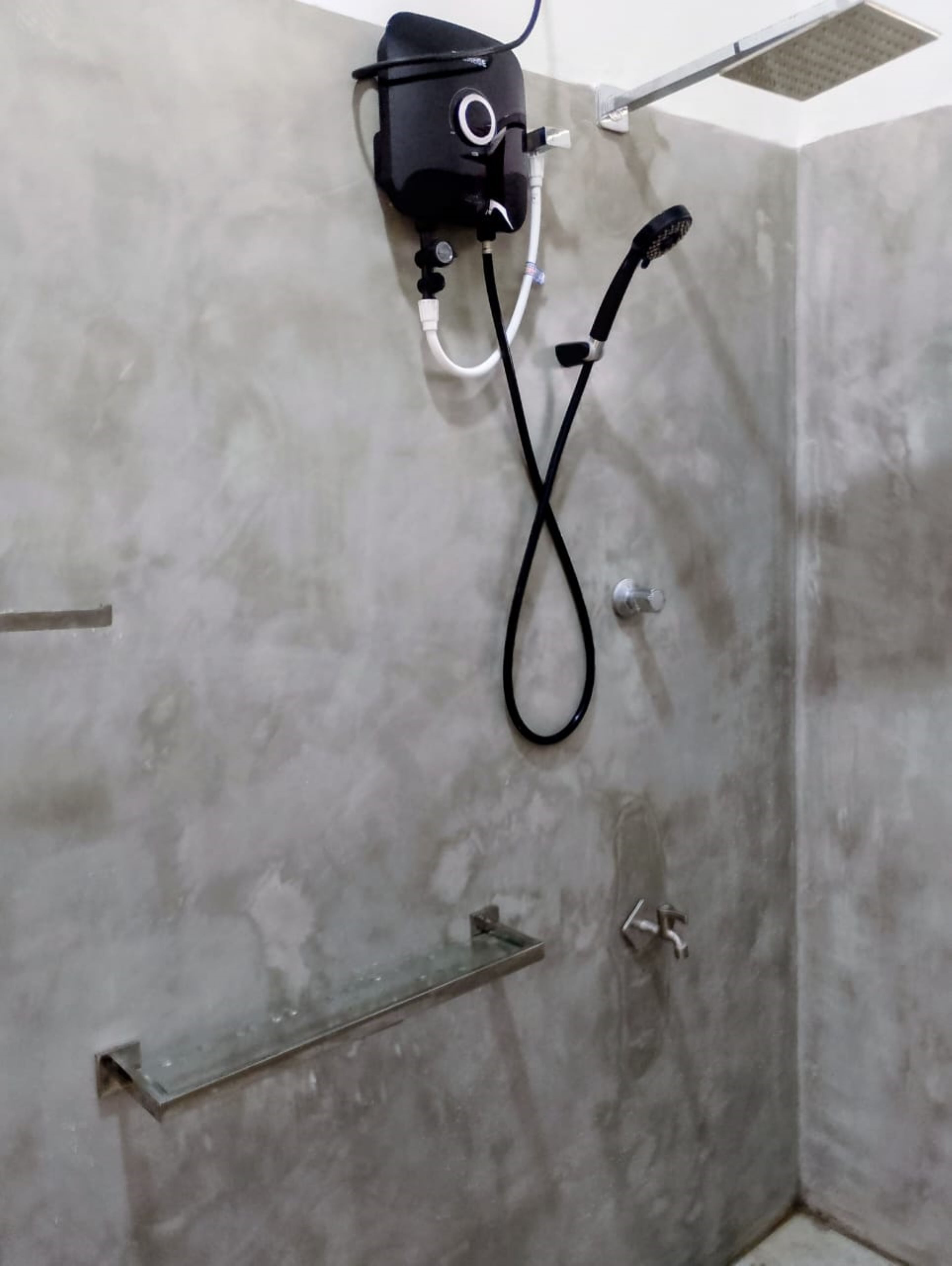 A shower area with a handheld showerhead, a control unit, and a metal shelf.