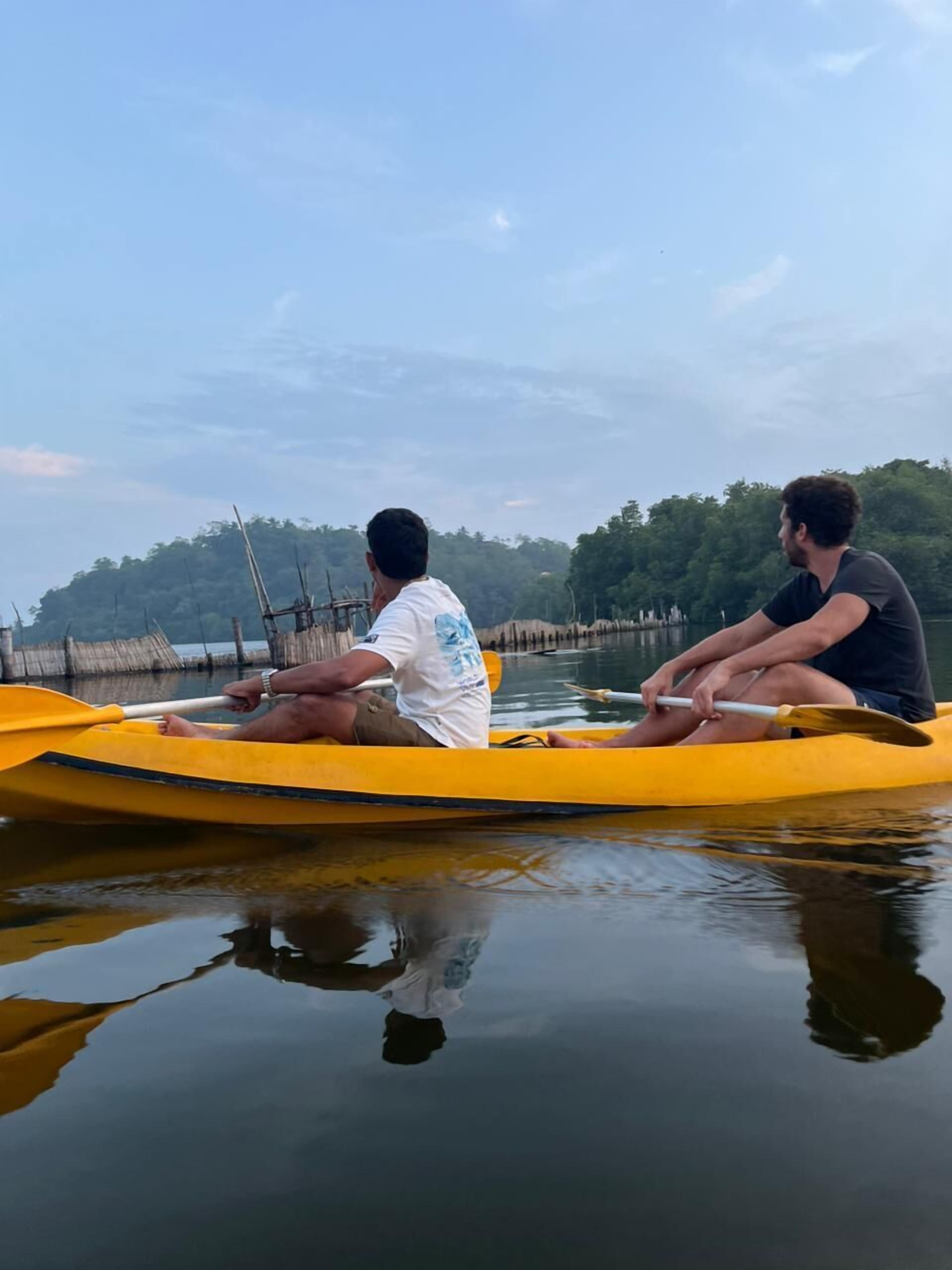 Two people in a yellow canoe on calm water with a forested shoreline in the background.