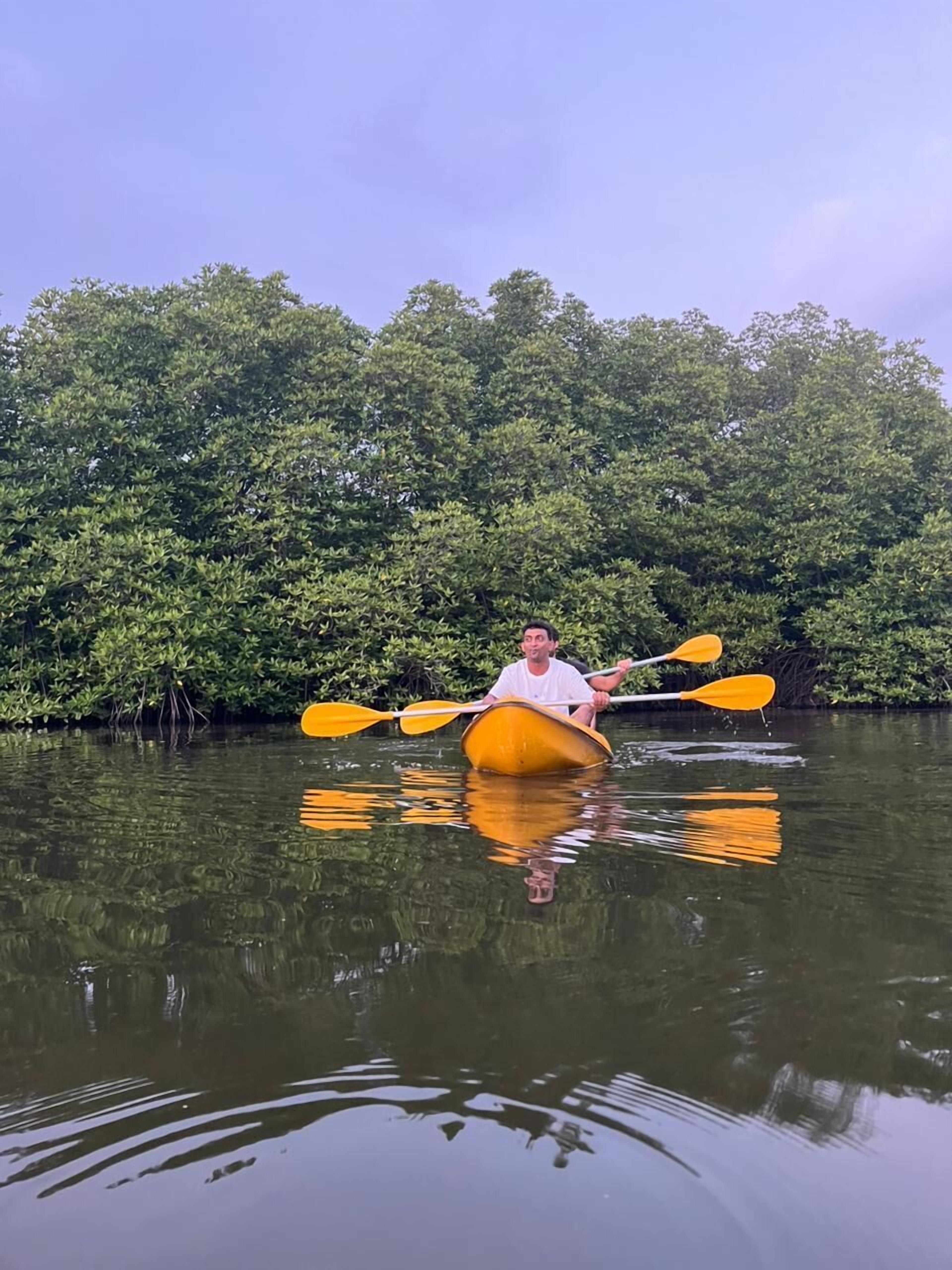 A person in a yellow kayak on calm water with dense green foliage in the background.