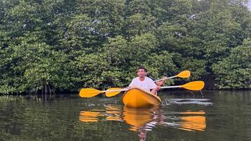 A person in a yellow kayak on calm water with dense green foliage in the background.