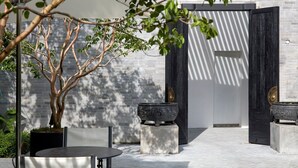 A modern outdoor patio with a minimalist design, featuring a tree, two large stone planters, and a sleek black gate. - Soori Penang (George Town)