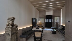 A modern interior with a stone lion sculpture, a seating area with cushions, a round table, and a television. - Soori Penang (George Town)