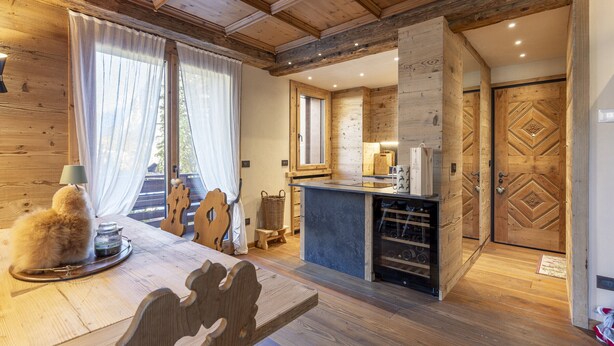 A cozy wooden interior with a dining area, a kitchen with a wine rack, and a large wooden door. - Casa Maddalena, comfort in Cortina d'Ampezzo (Cortina d´Ampezzo)