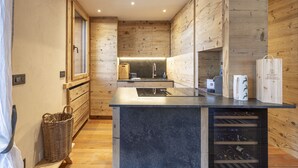 A modern kitchen with wooden paneling, a central island with a wine rack, and a built-in oven. - Casa Maddalena, comfort in Cortina d'Ampezzo (Cortina d´Ampezzo)