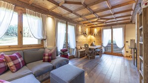 A cozy cabin interior with a wooden ceiling, a sofa with plaid cushions, a dining area, and large windows. - Casa Maddalena, comfort in Cortina d'Ampezzo (Cortina d´Ampezzo)