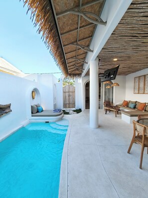 Zona de piscina con techo de paja, asientos y vistas al exterior.