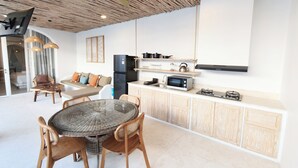 A modern kitchen with a central island, built-in appliances, and a dining area with wicker furniture. - Villa Vinodayan Uluwatu (Ungasan)