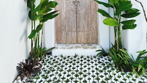 A white-walled entrance with a wooden door, a thatched roof, and tropical plants. - Villa Vinodayan Uluwatu (Ungasan)