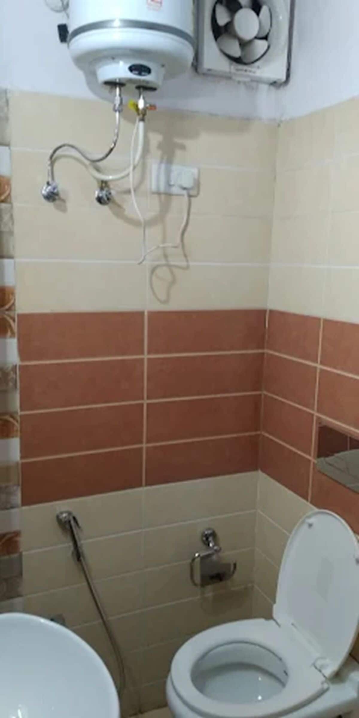 Un baño pequeño con inodoro, ducha y calentador de agua instalado en el techo.
