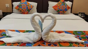 A hotel room with a bed featuring a heart-shaped towel arrangement and a colorful geometric-patterned bedspread. - Hotel Deepak Residency (Jaipur)