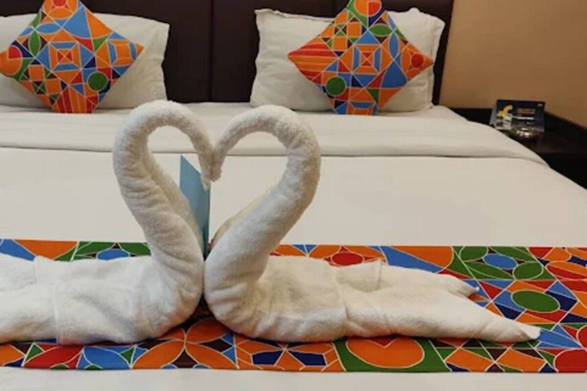 Une chambre d’hôtel avec un lit agrémenté d’une décoration en forme de cœur réalisée avec des serviettes, et une couvre-lit aux motifs géométriques colorés.