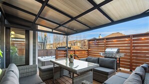 Een terras buiten met een tafel met glazen blad, rieten meubels en een barbecue.