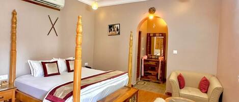 A bedroom with a four-poster bed, a ceiling fan, a wooden coffee table, a sofa, and a small table with a lamp.