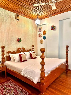 A neatly made bed with a wooden headboard, a patterned rug, and a ceiling fan. - Nimbal Dhani (Jaipur)