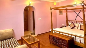 A bedroom with a four-poster bed, a ceiling fan, a glass coffee table, a sofa, and a wooden bench. - Nimbal Dhani (Jaipur)