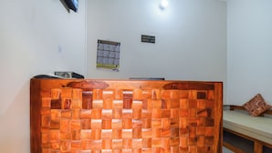 A reception desk with a woven wood design, a wall-mounted clock, and a sign indicating check-out and check-in times. - Nimbal Dhani (Jaipur)