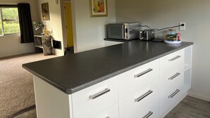 Una cocina moderna con encimera oscura, armarios blancos y un tostador. Se observa una ventana con vistas a la vegetación.