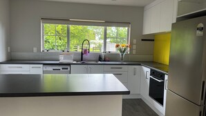 Una cocina moderna con un amplio ventanal, armarios blancos, un refrigerador de acero inoxidable y una encimera negra.