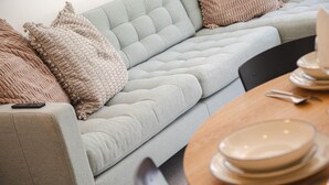 Un soggiorno moderno con un divano grigio chiaro, cuscini beige e un'area pranzo con un tavolo di legno apparecchiata per due.