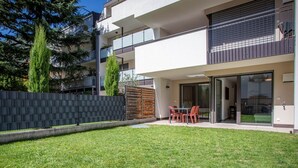 Un edificio residenziale moderno di due piani con tetto piatto, ampie finestre a vetro e un piccolo patio con tavolo e sedie.