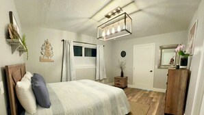 Et soveværelse med en stor seng, en trækommode, et spejl og en loftlampe.