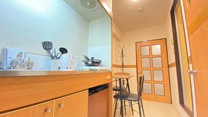 A compact kitchen with a wooden countertop, a coffee maker, and a kettle. There is a dining area with a table and chairs, and a door with frosted glass panels. - 30sec walk to Tsutenkaku/1 stop to Namba Sta./AH23 (Ebisu Higashi Naniwa Ward,Osaka City)