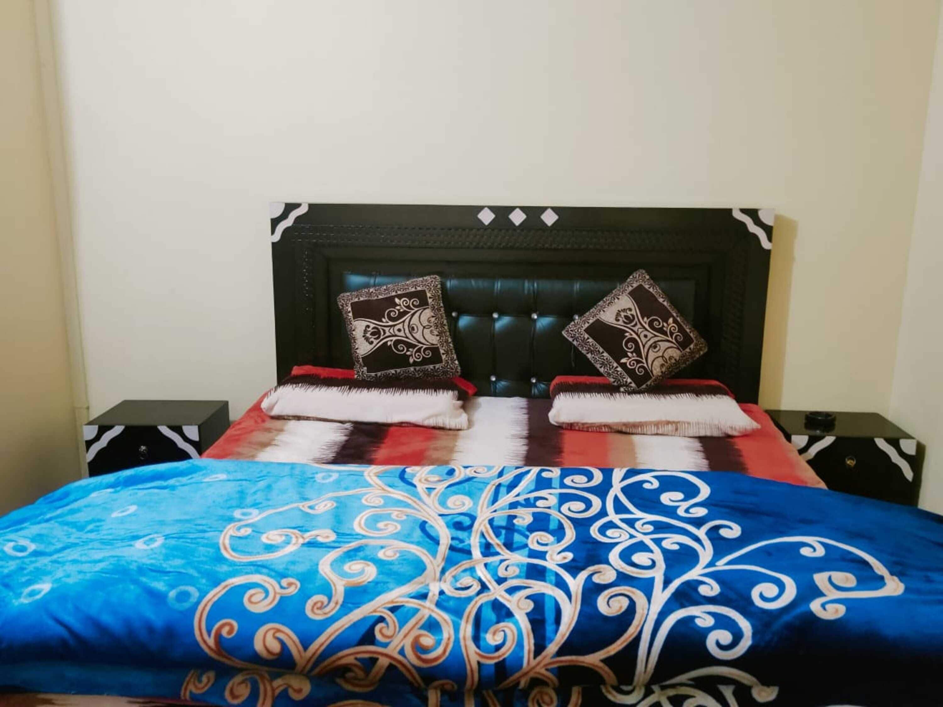 A bed with a blue and red patterned bedspread, two decorative pillows, and a dark headboard.