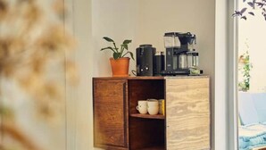 Un meuble en bois, avec une plante et une machine à café posées sur le dessus, et une étagère avec des tasses.
