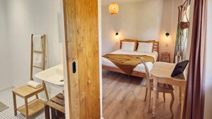 Une chambre avec un lit en bois, une table de chevet et un ordinateur portable. On y trouve également une chaise en bois et une petite table de chevet avec une lampe.