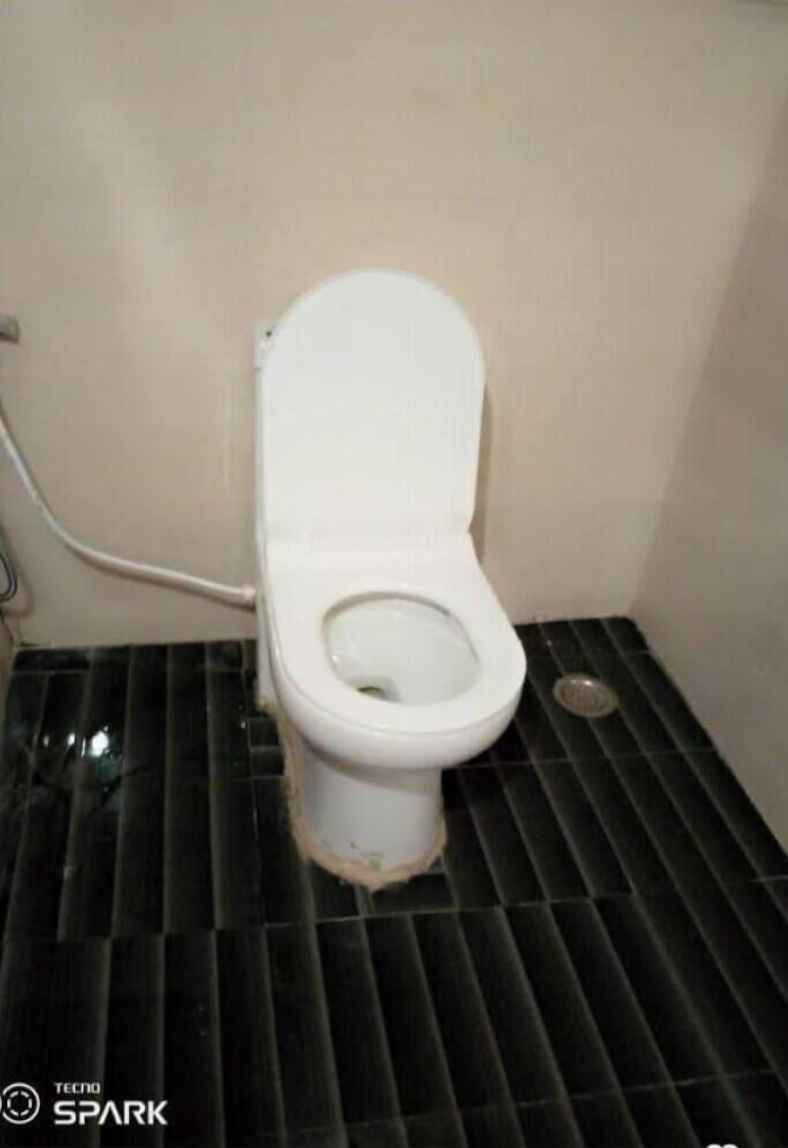 A toilet with a white seat and lid, positioned in a small room with a black tiled floor.