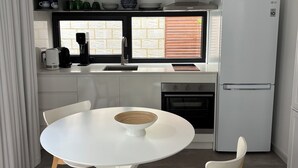 A modern kitchen with a white table and chairs, a built-in oven, and a refrigerator. - Coogee Beach House. Sunsets and yellow sand. 2 minutes to the ocean. (Coogee)