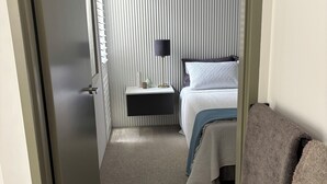 A narrow hallway leading to a bedroom with a bed, bedside table, lamp, and a window with blinds. - Coogee Beach House. Sunsets and yellow sand. 2 minutes to the ocean. (Coogee)