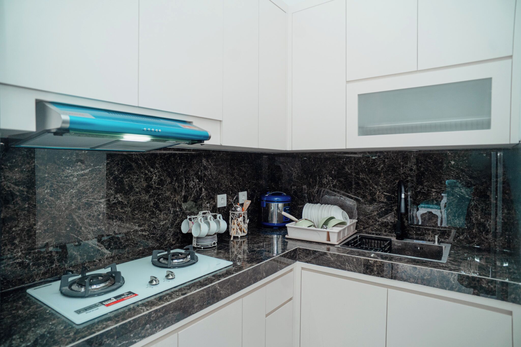 A modern kitchen with a gas stove, a blue range hood, and white cabinets.
