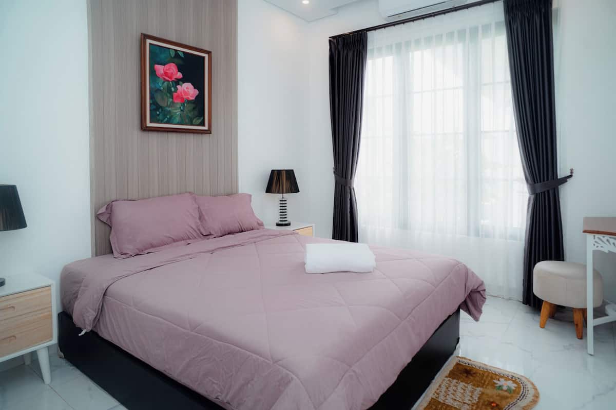 A neatly arranged bedroom with a bed, bedside table, lamp, and a painting on the wall.